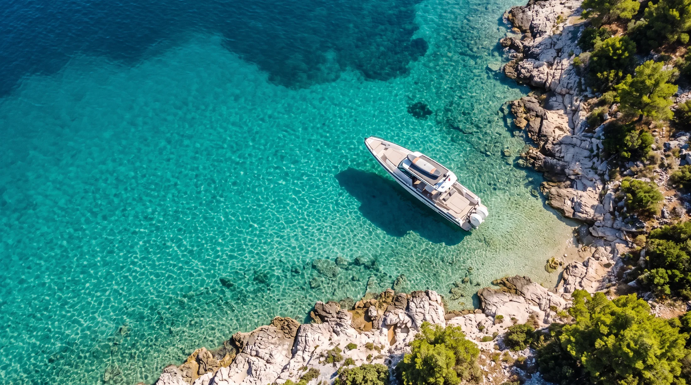 The boat at anchor in a clear turquoise cove, seen from above.
